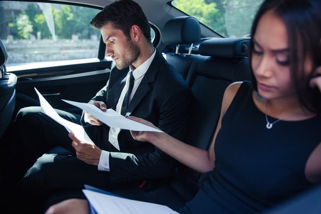 Businesswoman and businessman reading papers on back seat in car